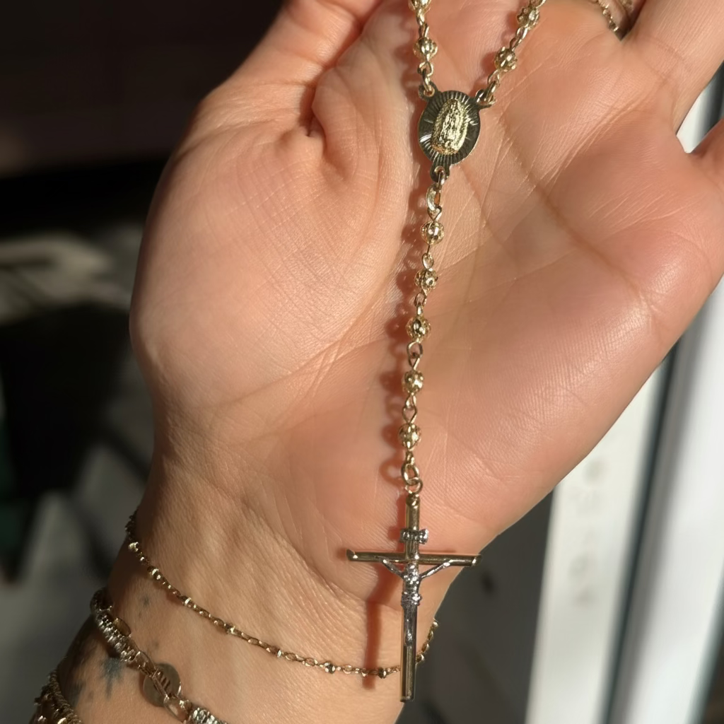 Hand holding a solid gold rosary with a cross, surrounded by other bracelets.