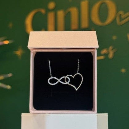 Necklace with heart and infinity symbol in a box against a festive green background