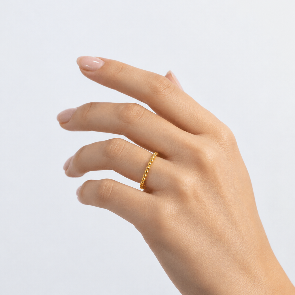 Hand wearing a gold ring on a light gray background