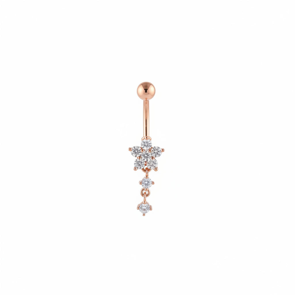 A hand with pink manicured nails holds a rose gold dangle earring with a flower-shaped crystal charm in front of a blurred boutique interior.