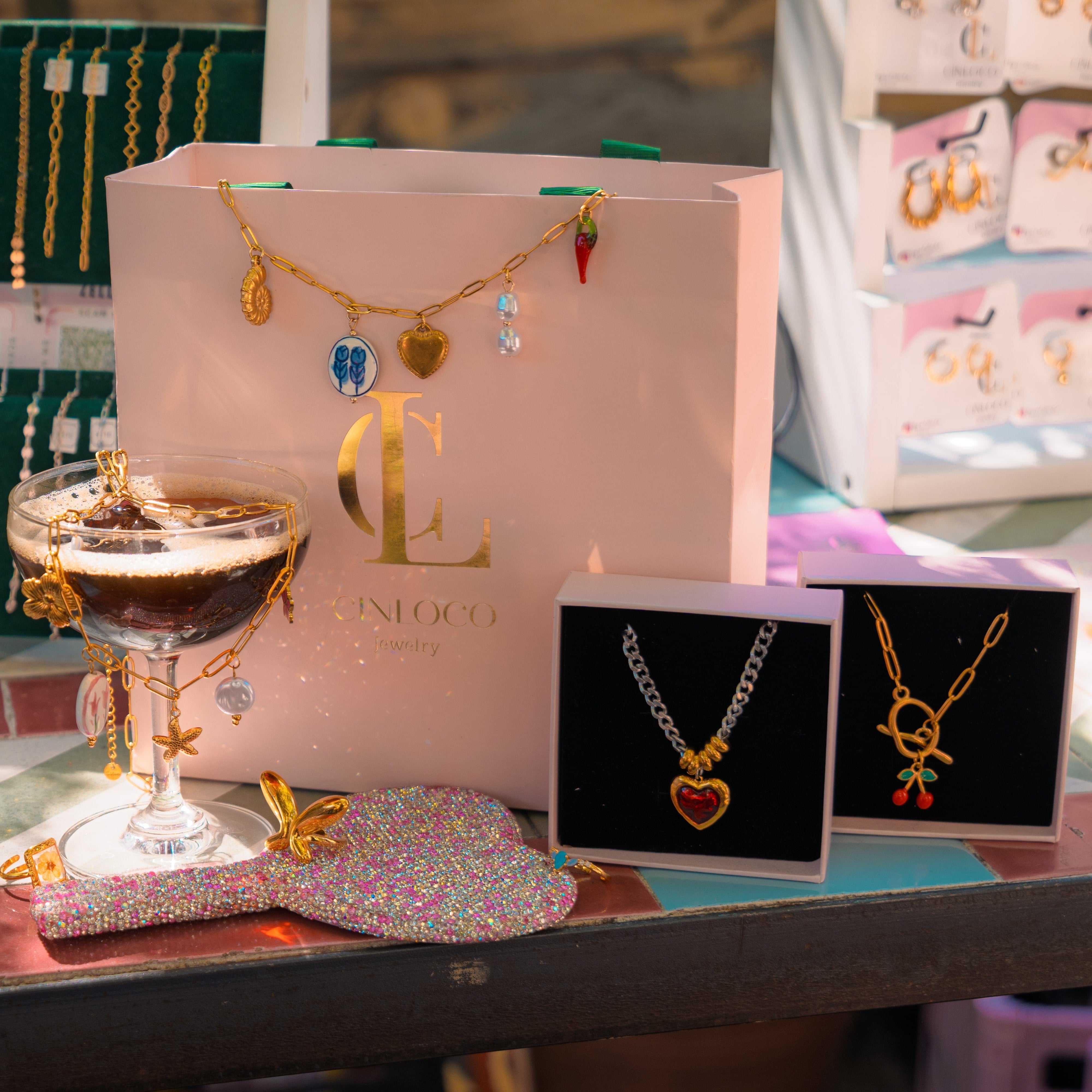 Jewelry display with necklaces, a glass of coffee, and a branded bag on a table.