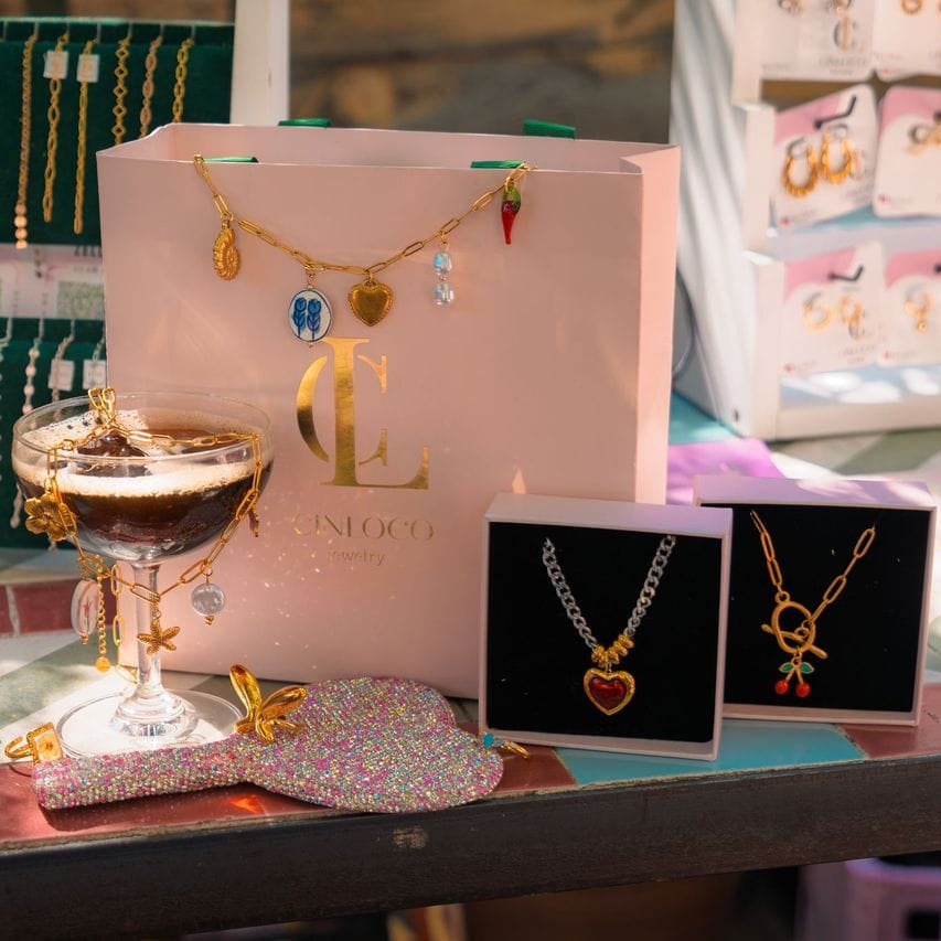 Jewelry display with necklaces, a glass of coffee, and a branded bag on a table.