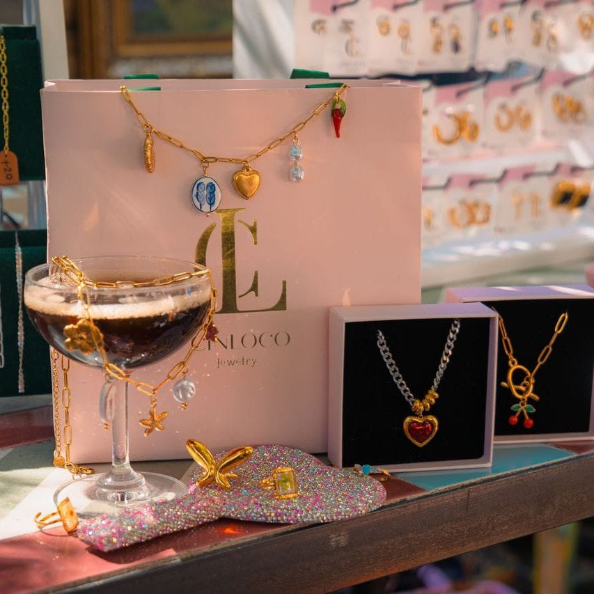 Jewelry display with necklaces, a glass of wine, and a pink box on a table.