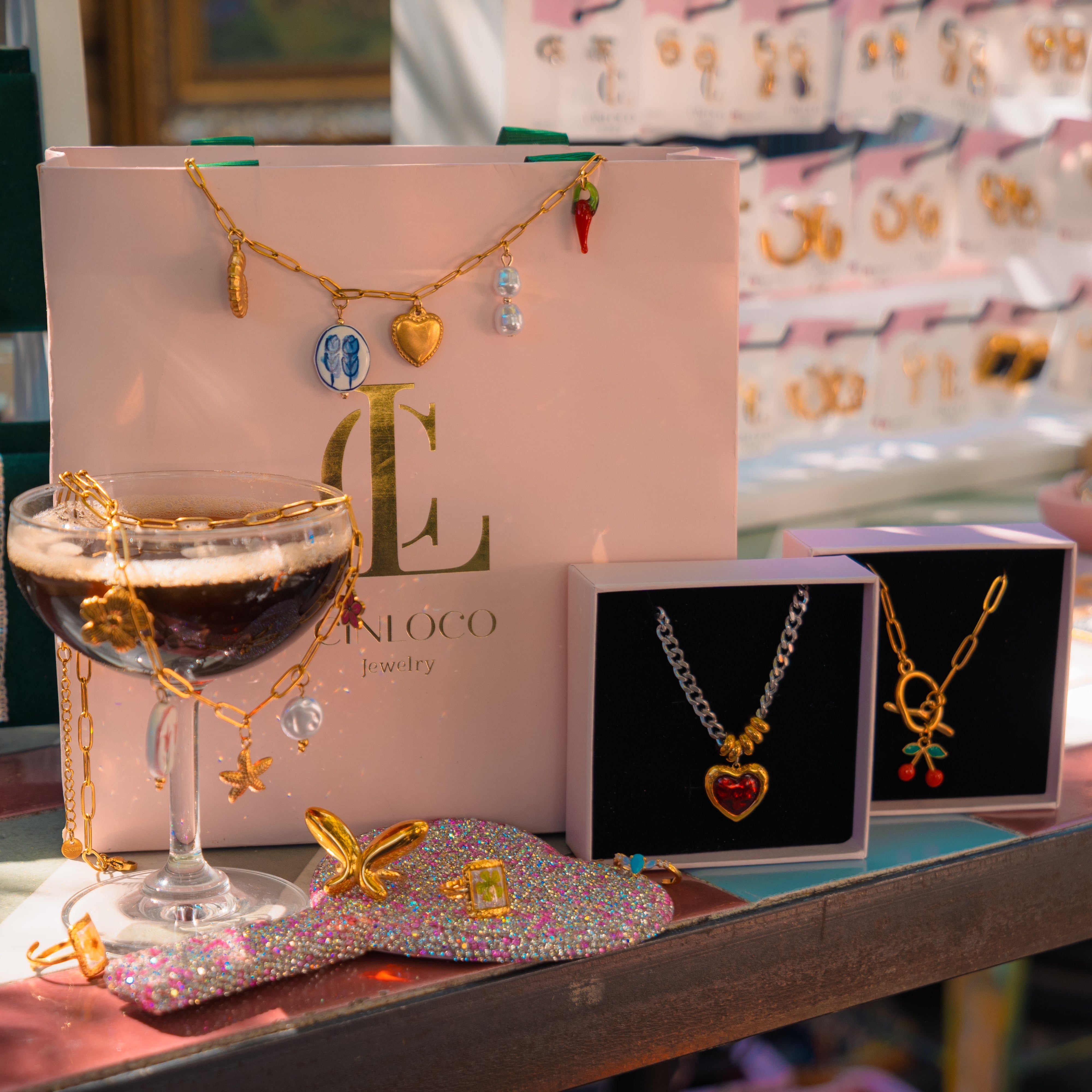 Jewelry display with necklaces, a glass of wine, and a pink box on a table.