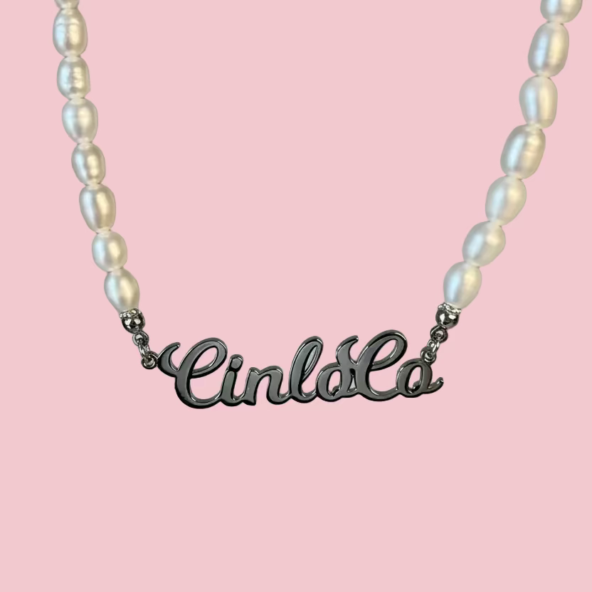 Pearl necklace with a silver 'Cinlola' pendant on a light gray background