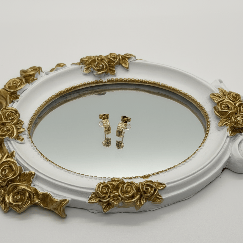 Decorative tray with gold floral designs containing a pair of earrings on a white background