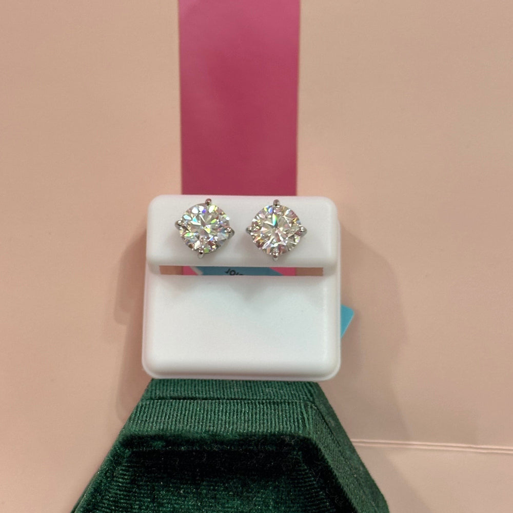 Pair of silver earrings in a white display case with a green jewelry box featuring a logo on a pink background.