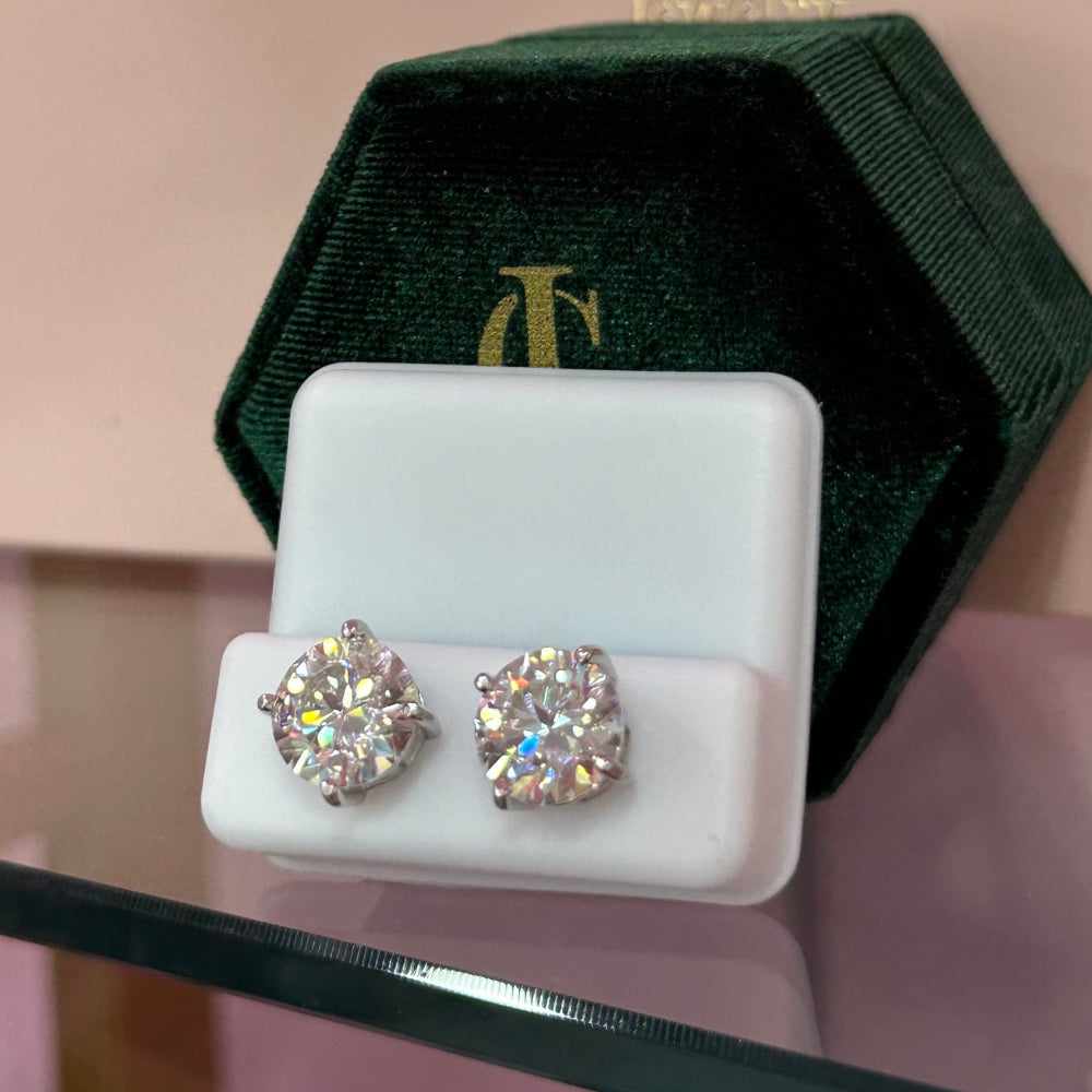 Diamond earrings in a green and gold box with Clinique logo on a pink background