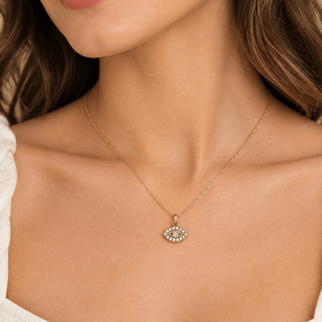 A close-up lifestyle shot of a woman wearing a delicate gold chain necklace with a small eye-shaped pendant set with clear stones.