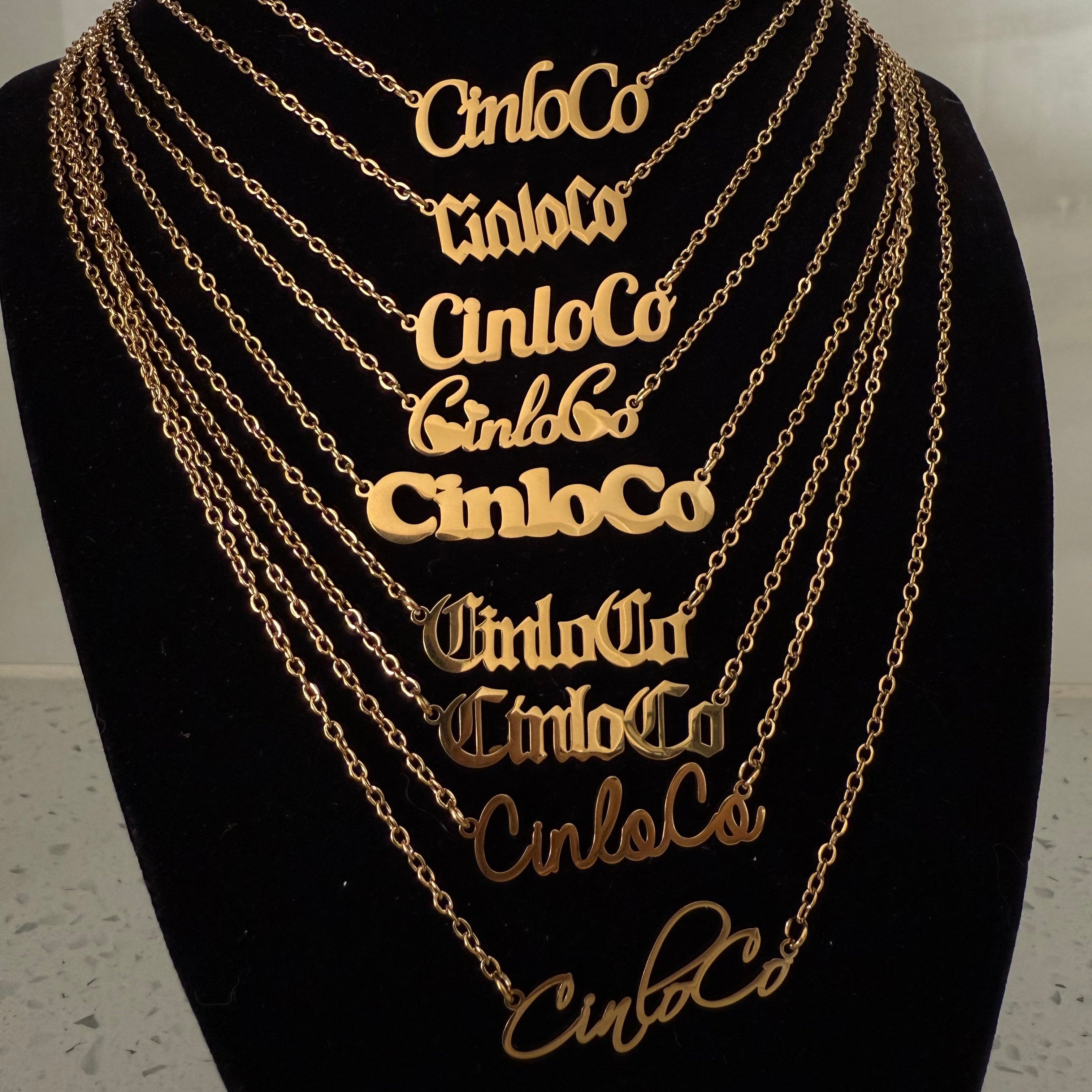 Gold chain necklaces with custom name plate branding on a black mannequin.