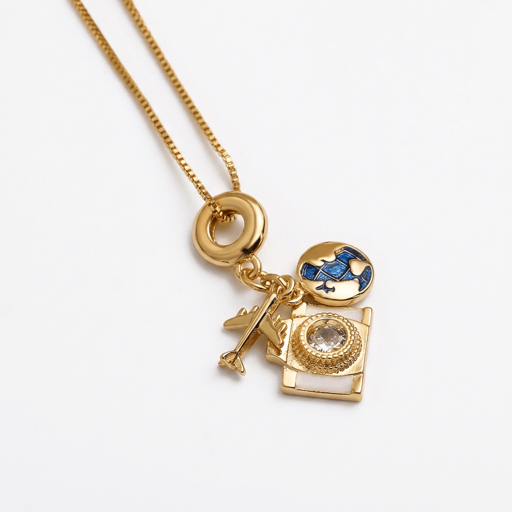 A gold-tone chain necklace with a multi-charm pendant featuring a camera, an airplane, a globe, and a ring, photographed on a clean white background.
