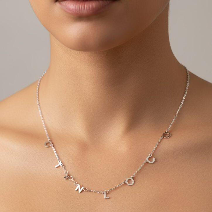 Silver necklace with letter pendants on a person's neck against a neutral background