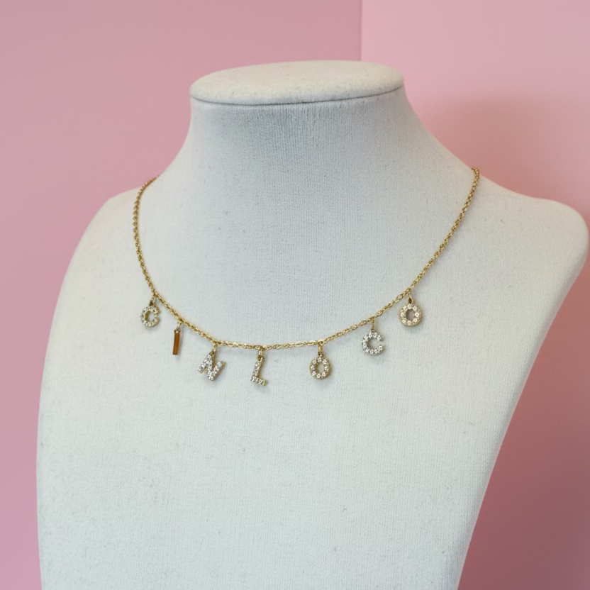 Gold necklace with various charms on a mannequin bust against a plain background