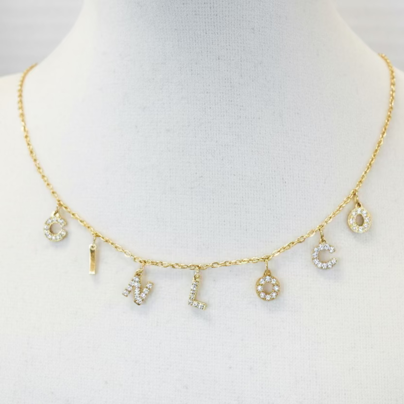 Gold necklace with charms on a mannequin bust against a gray background