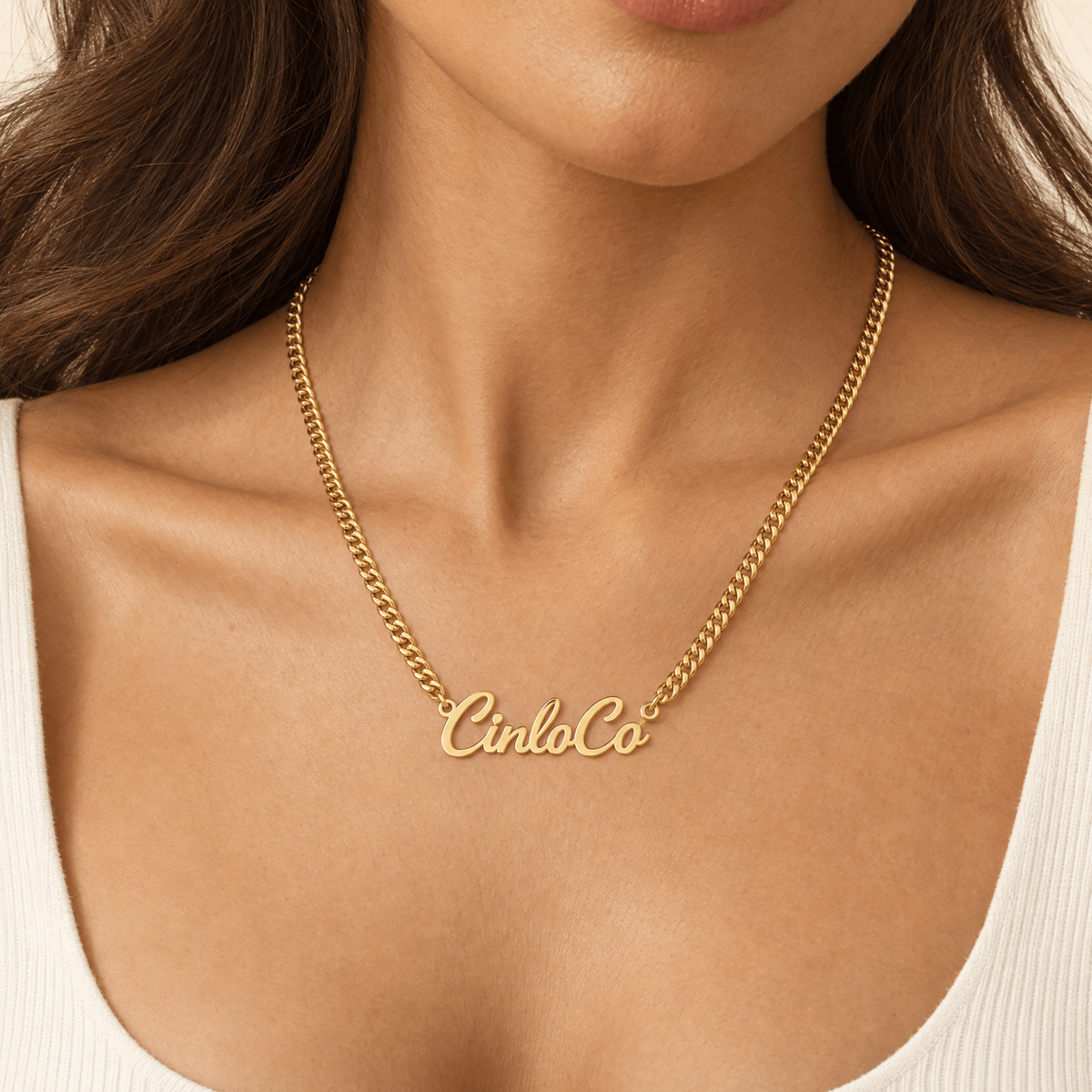 A close-up of a model wearing a gold chain necklace with a personalized script nameplate reading 'CincoCo'.