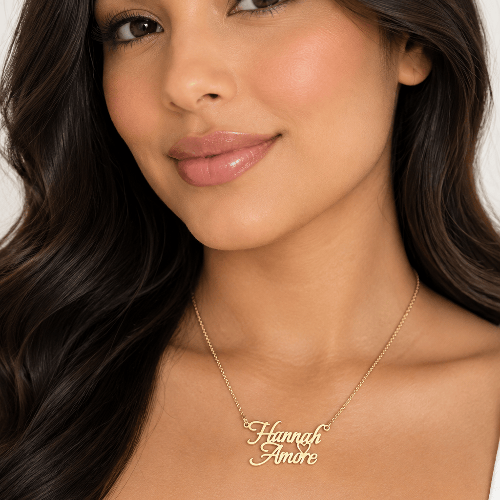 A gold nameplate necklace reading 'Hannah Amore' with a small heart detail, suspended from a gold chain on a plain white background.