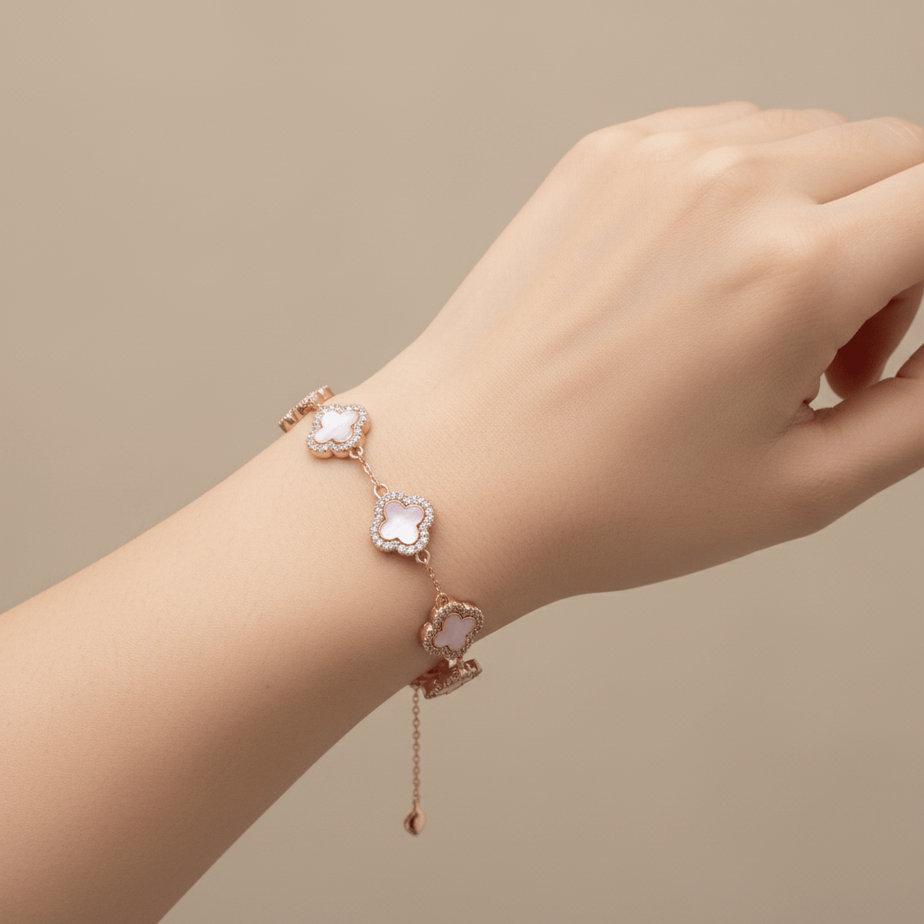 A delicate rose gold bracelet with three clover-shaped charms, each featuring a pale pink stone, shown worn on a person's wrist against a soft beige background.