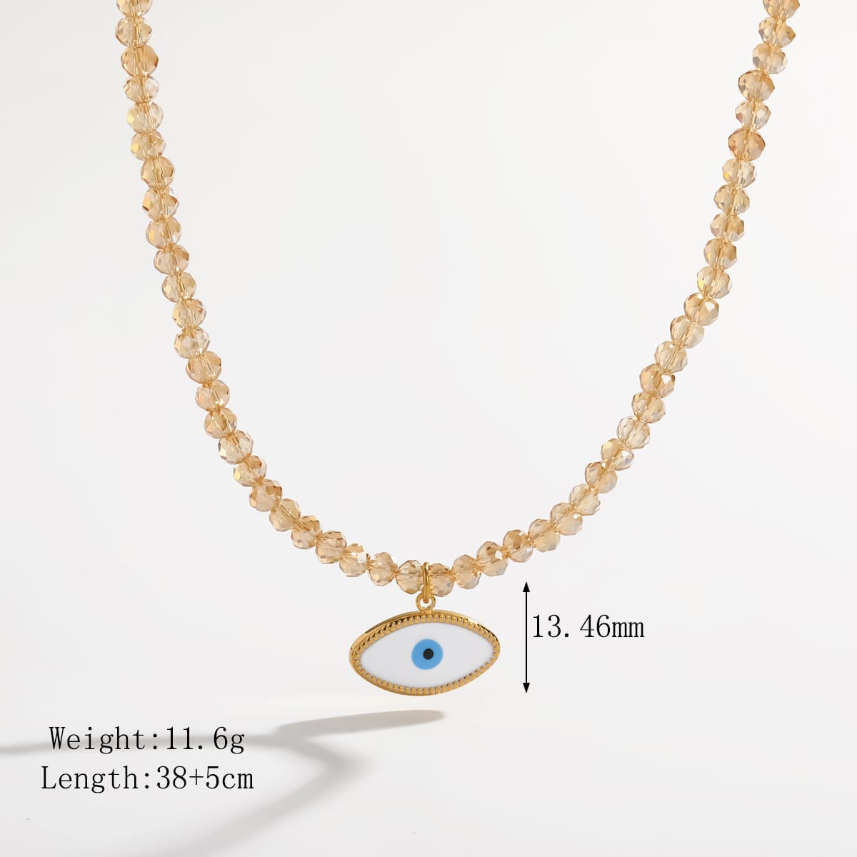A gold-toned beaded necklace with a white oval evil eye pendant featuring a blue center, shown on a light gray background with text indicating weight, length, and height measurement.