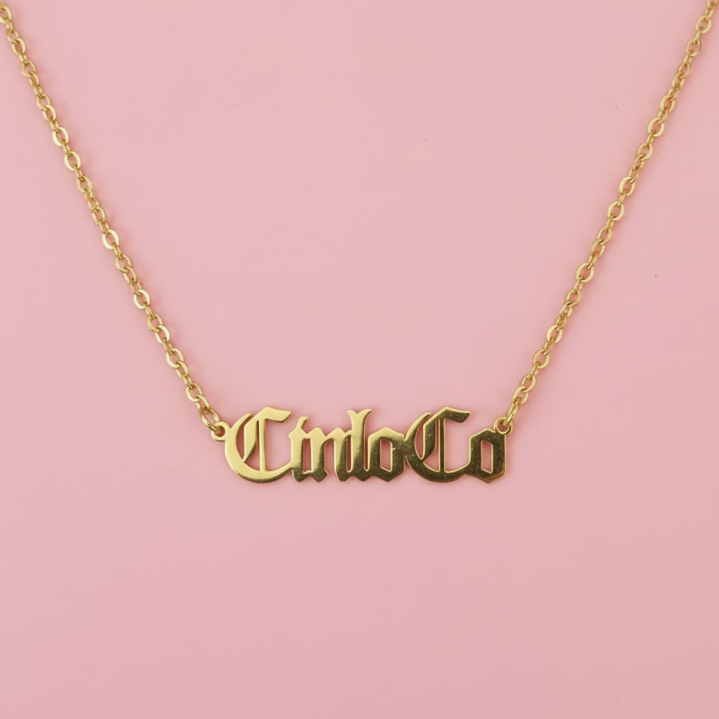 Gold necklace with 'CincoCo' pendant on a black background