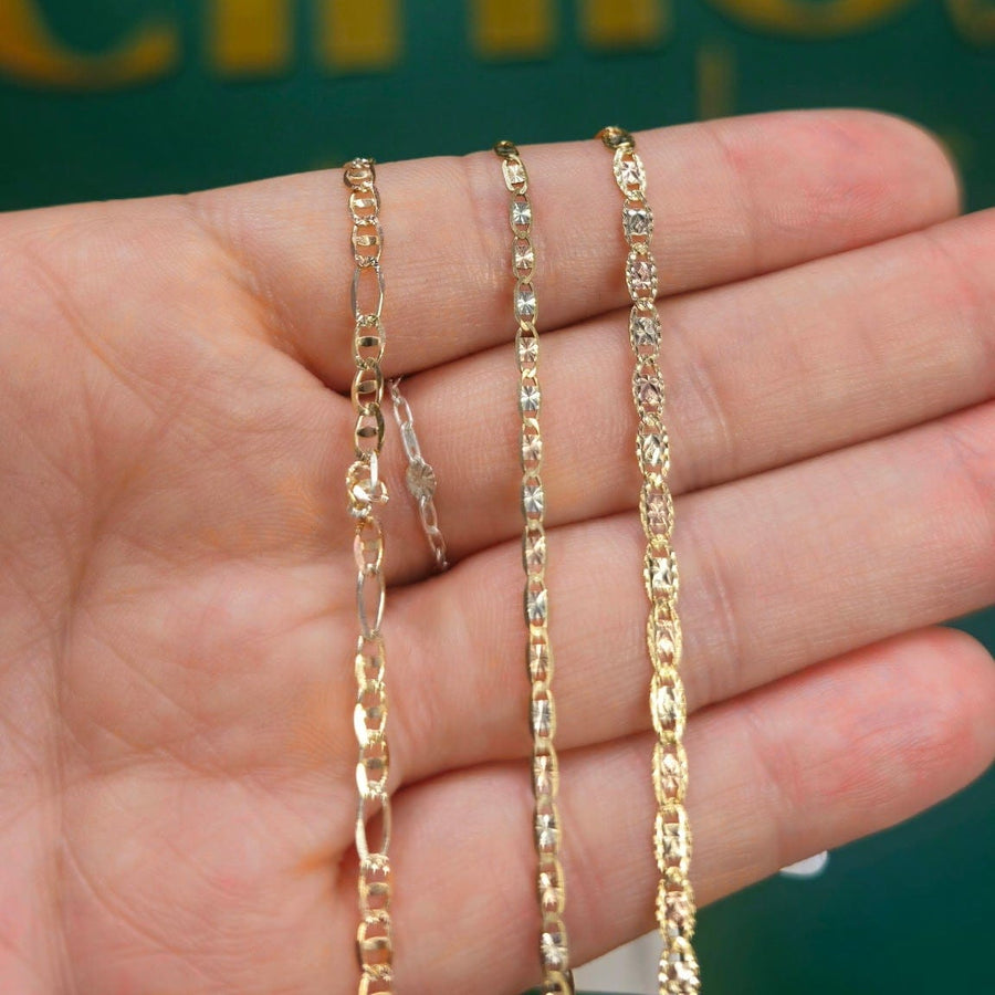 Two gold-tone chain necklaces, one curb link and one paperclip link, held in a person's hand against a dark green background with gold lettering.