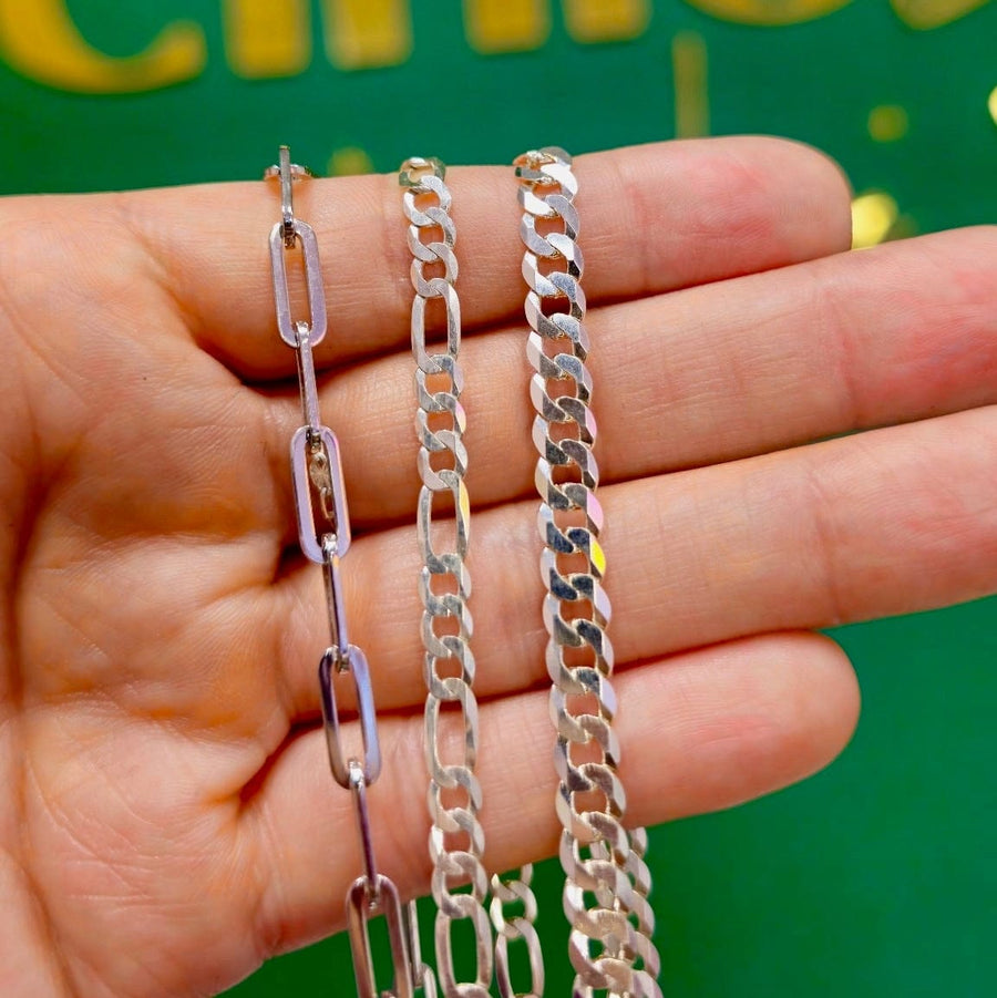 Three silver-toned chain necklaces in different link styles held in a person's hand against a green background with gold lettering.