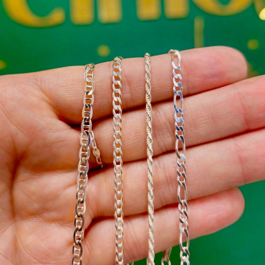 A hand holding four different metallic chain necklaces in gold, silver, and rose gold tones against a green background with gold lettering.