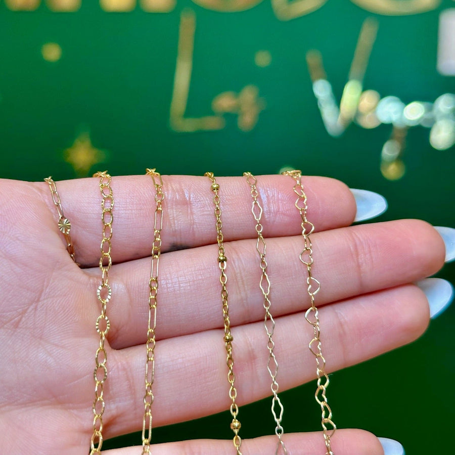 Four delicate gold chain necklaces displayed on a person's hand, with a green background featuring gold metallic lettering.