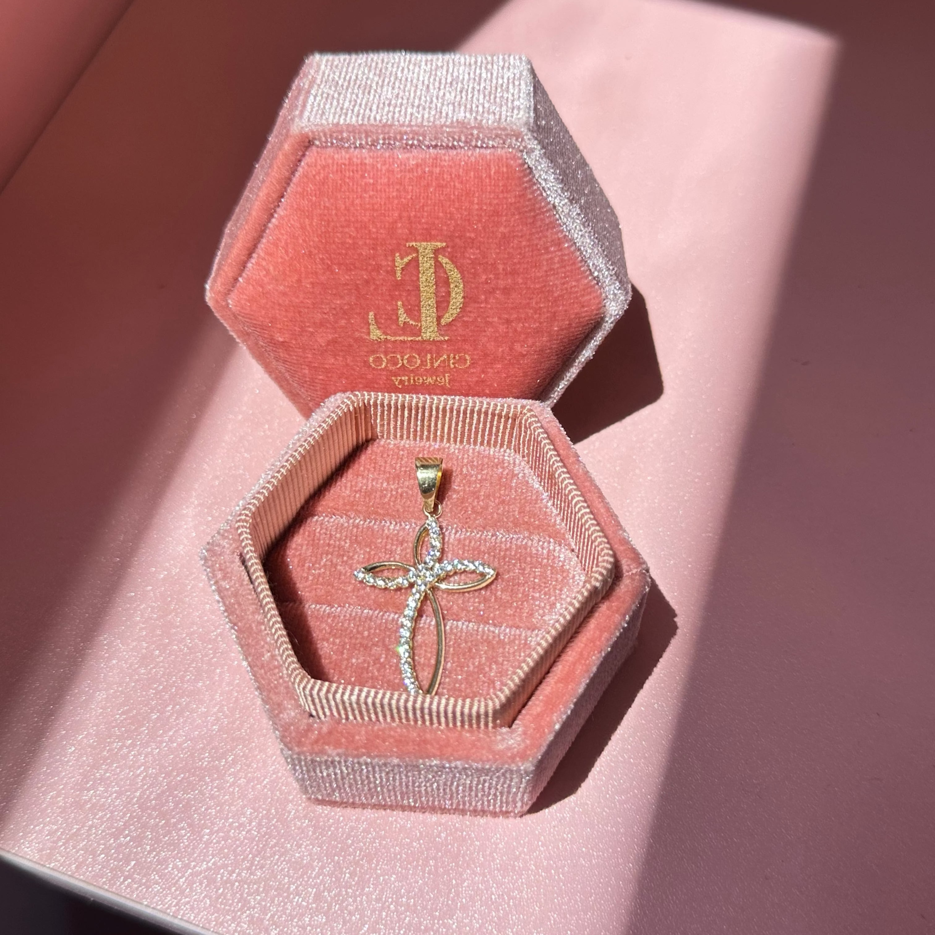 Gold cross pendant in a pink jewelry box with 'CinloCo' branding on a pink background