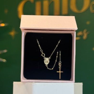 Gold necklace with a cross pendant in a pink box on a green background