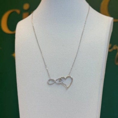 10K SOLID GOLD WHITE GOLD Necklace with a heart and infinity symbol on a mannequin bust against a green background.