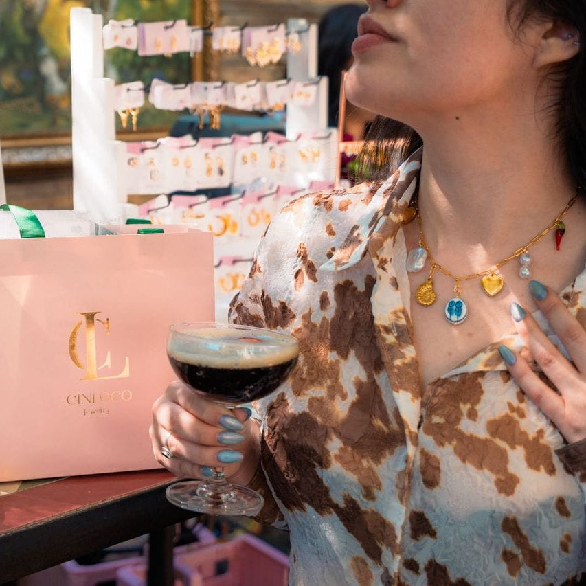 Woman holding a glass of coffee with jewelry on display in the background