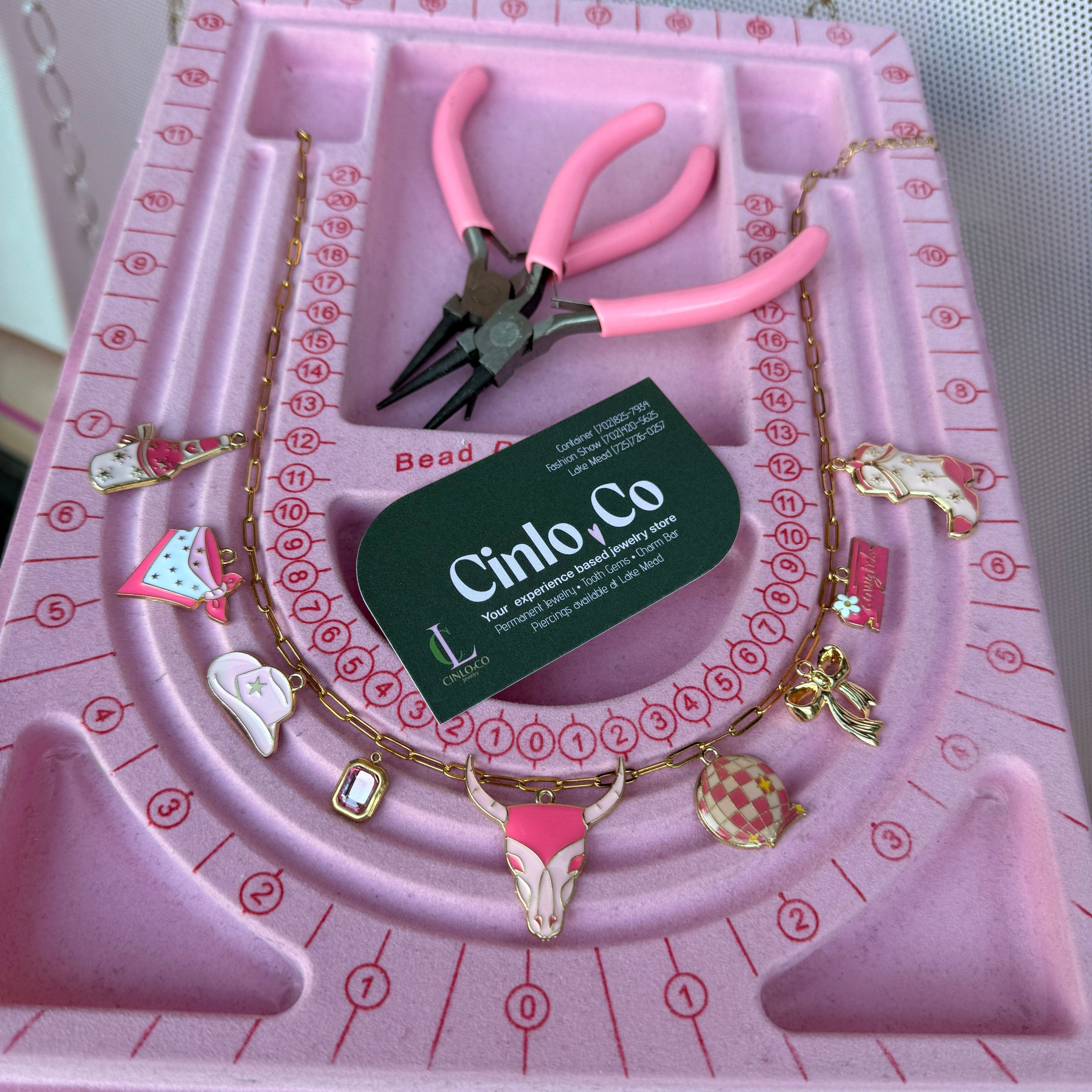 Pink jewelry-making kit with tools and charms on a pink tray
