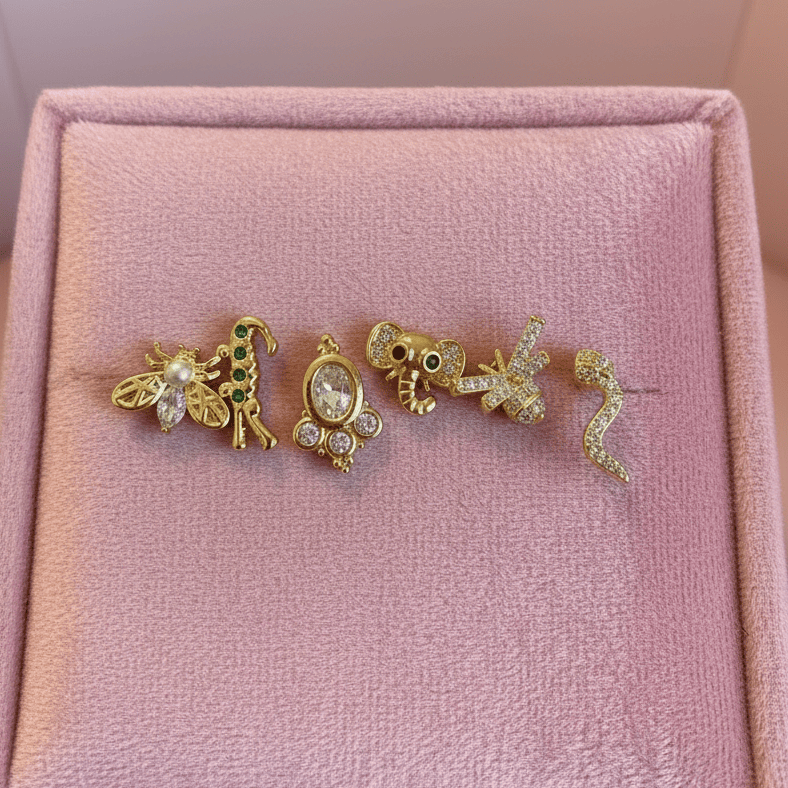 Three gold animal-shaped earrings on a pink jewelry box