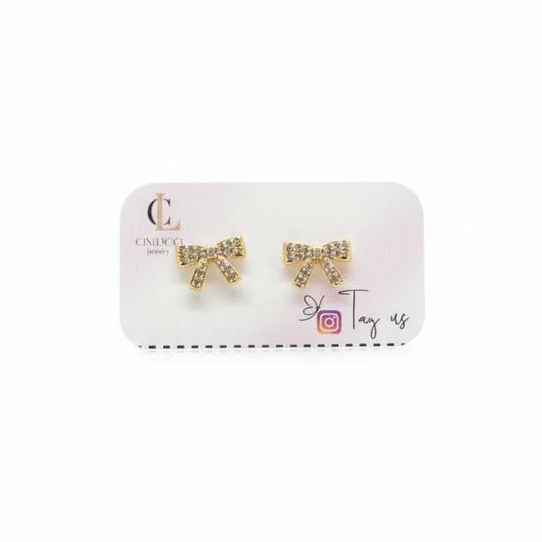 Earring packaging with a pink jewelry box and gold bow earrings, set against a decorative background with flowers and jars.