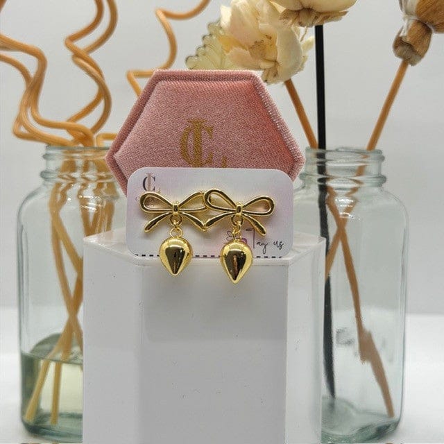 Gold bow-shaped earrings on a display card with a decorative background