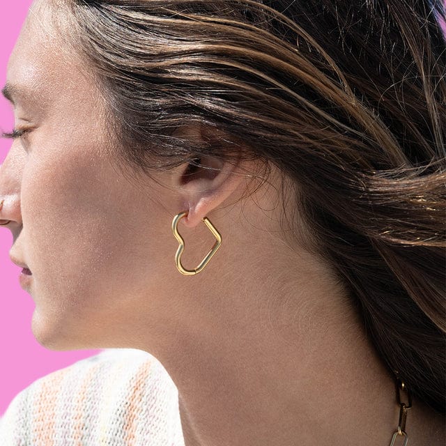 Close-up of a woman wearing a gold heart hoop earring with a blurred background