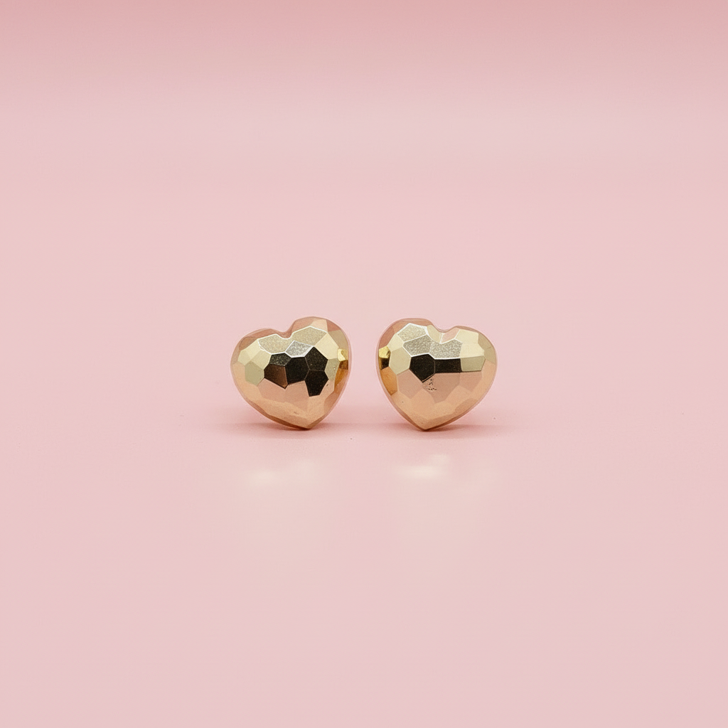 Gold heart-shaped earrings on a branded card with a pink jewelry box in the background.