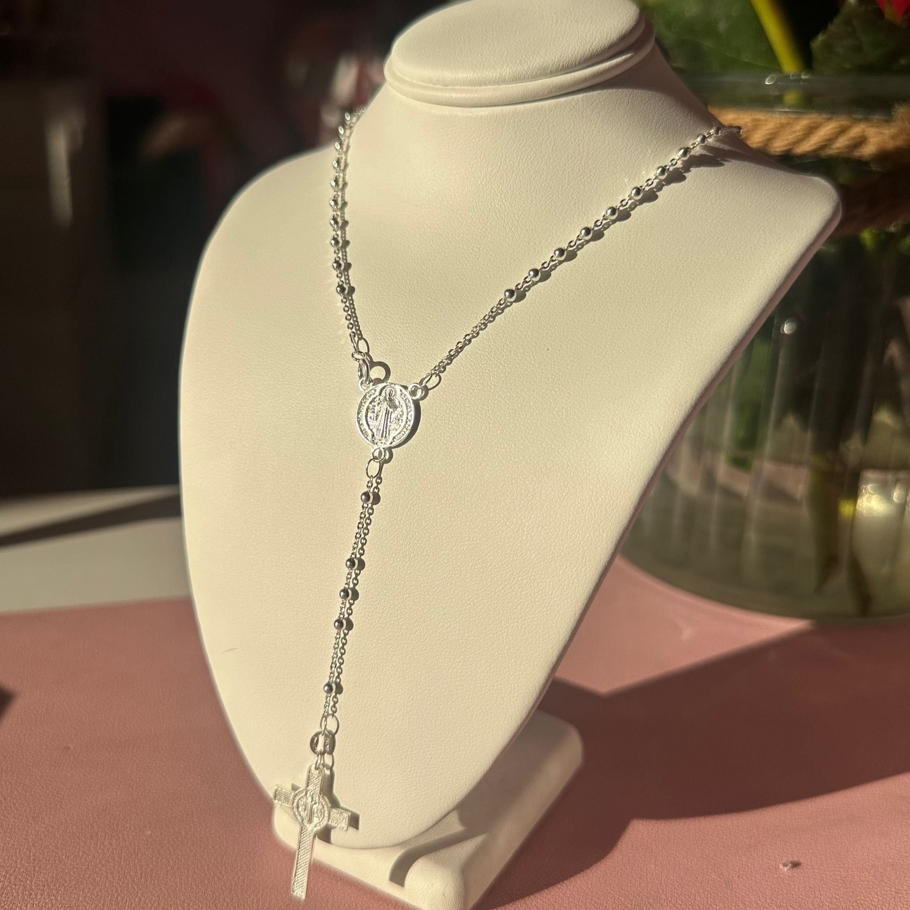 sterling Silver rosary necklace on a white bust with flowers in the background