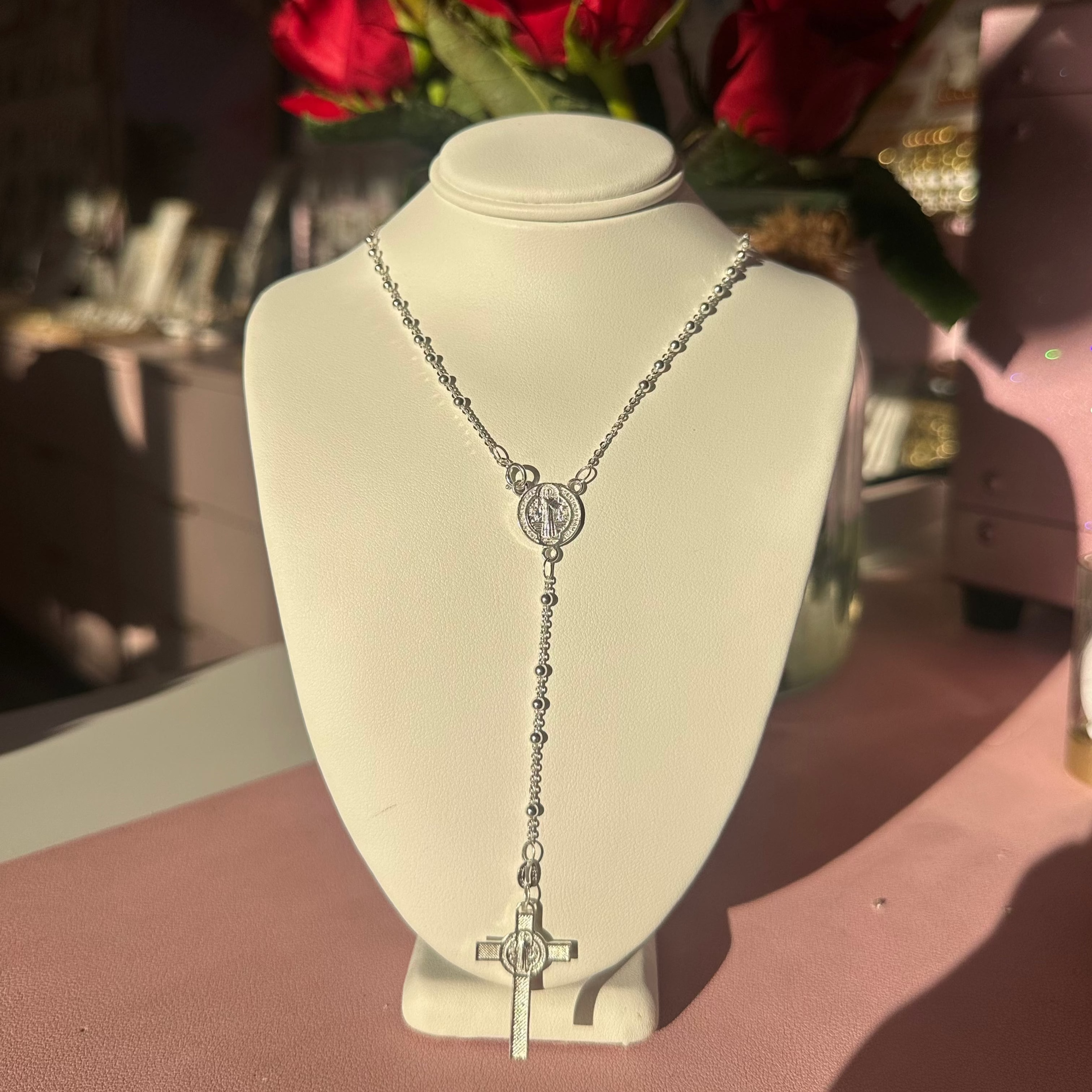 Silver rosary necklace on a mannequin bust with red roses in the background