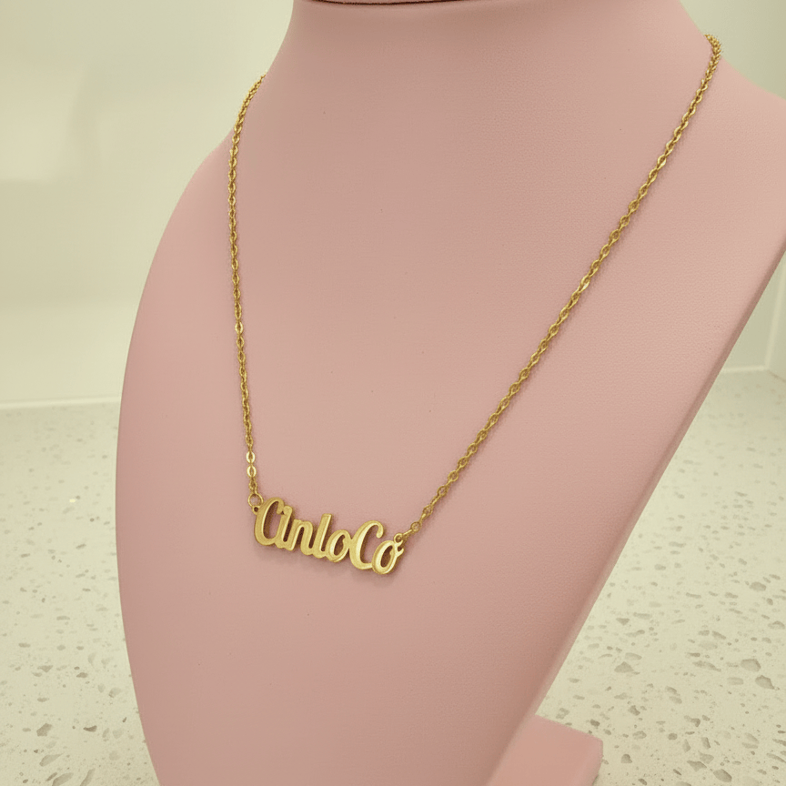 Gold name necklace with 'Cinco' pendant on a pink stand