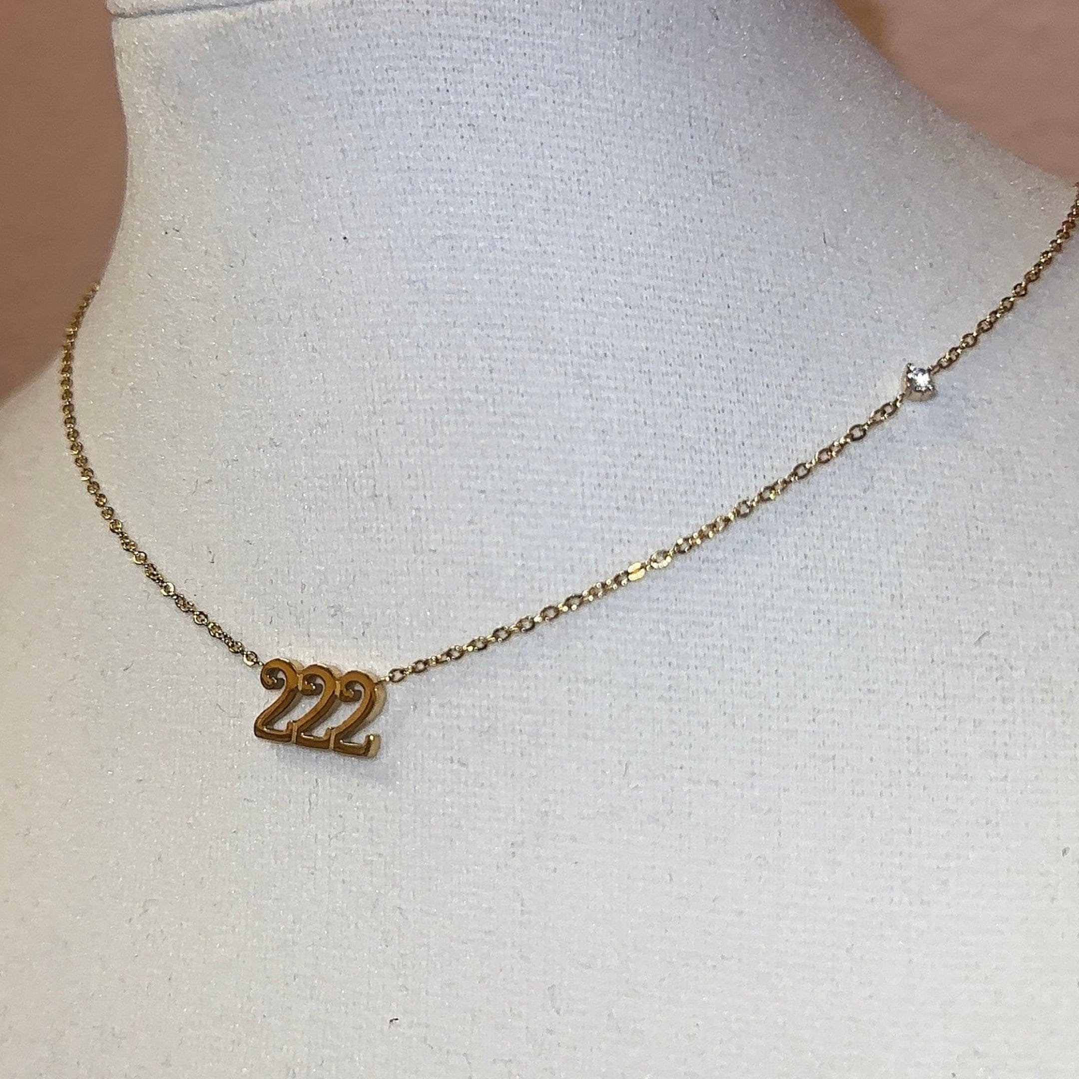 Gold necklace with a 222 pendant on a mannequin bust against a pink wall.