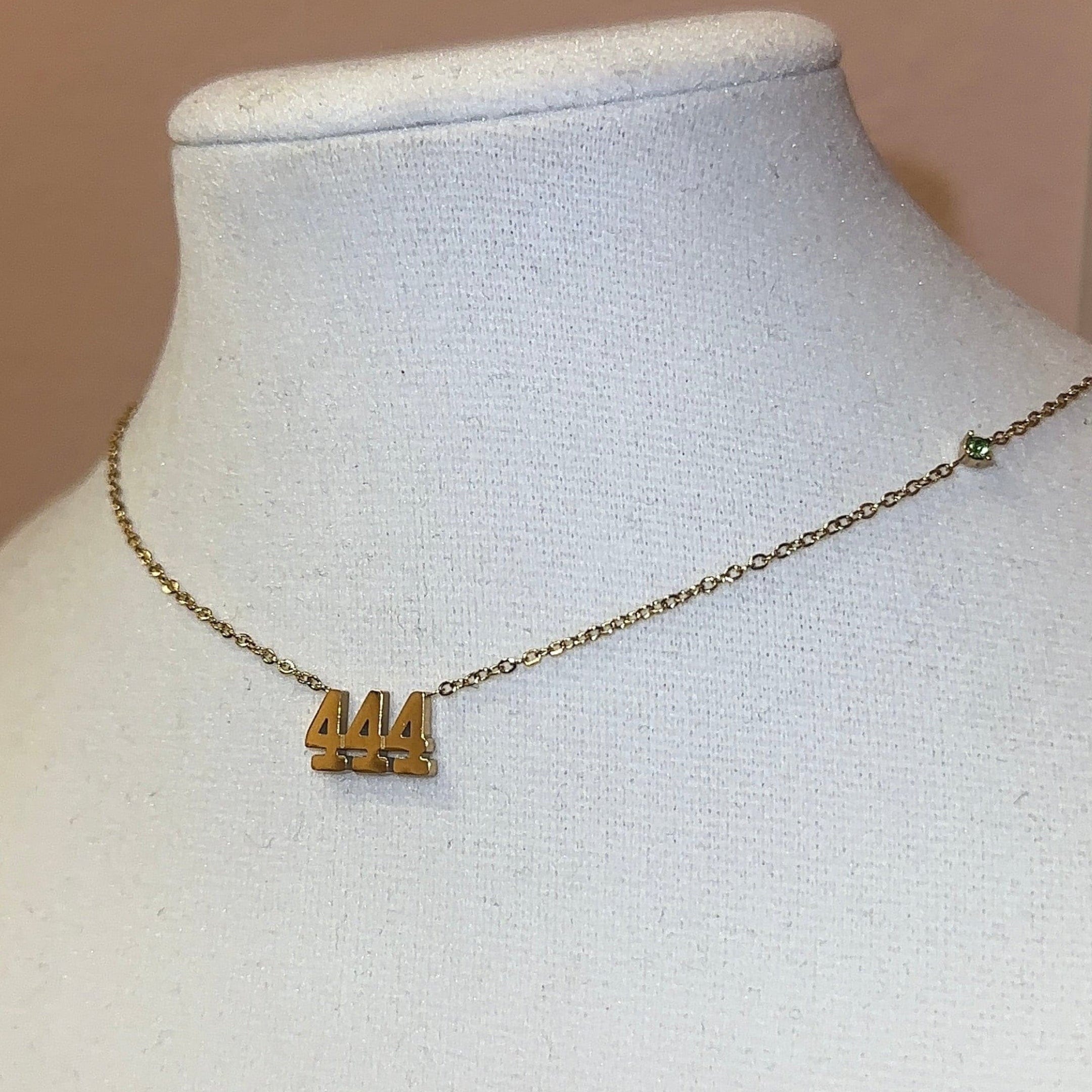 Gold necklace with a small pendant on a mannequin bust against a pink wall.