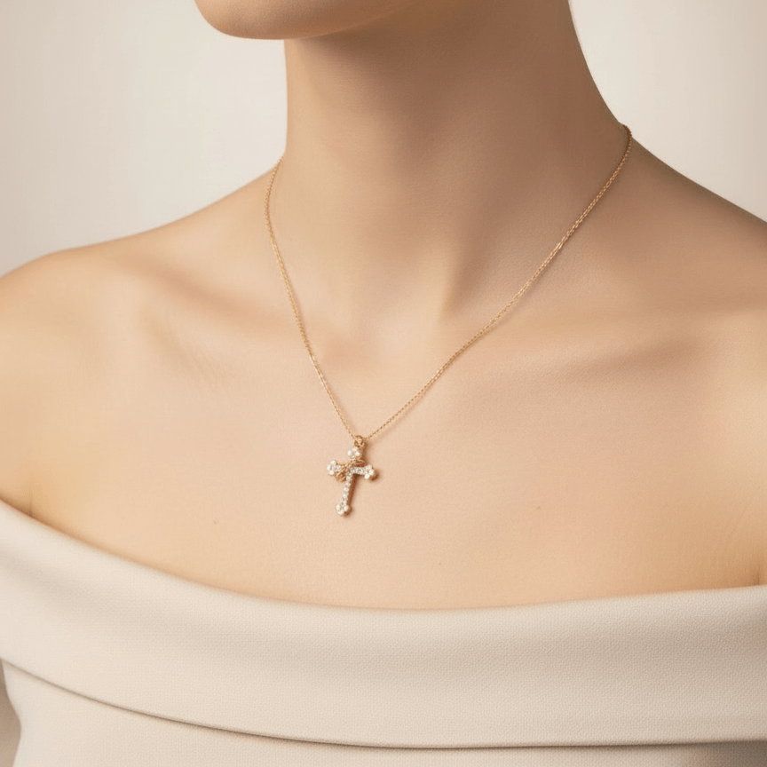 Gold necklace with a cross pendant worn by a person against a neutral background