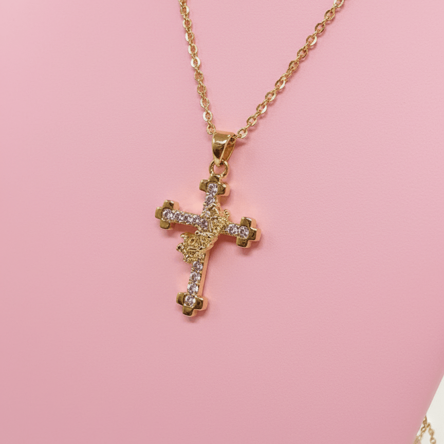 Gold cross necklace with clear stones on a pink background