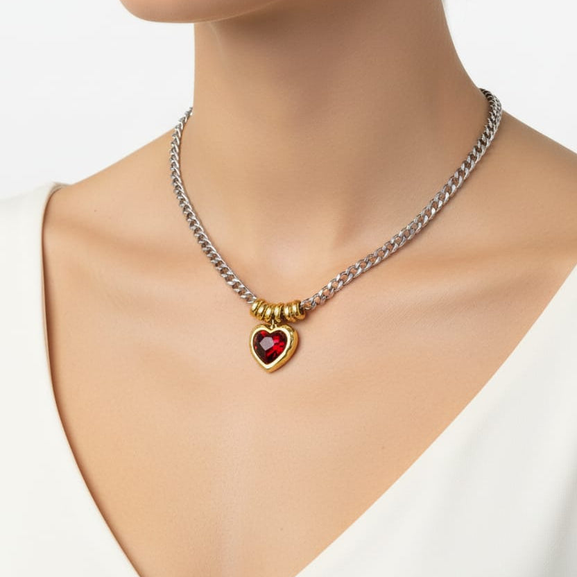 A close-up of a woman wearing a silver chain necklace with a gold heart-shaped pendant featuring a red heart in the center.