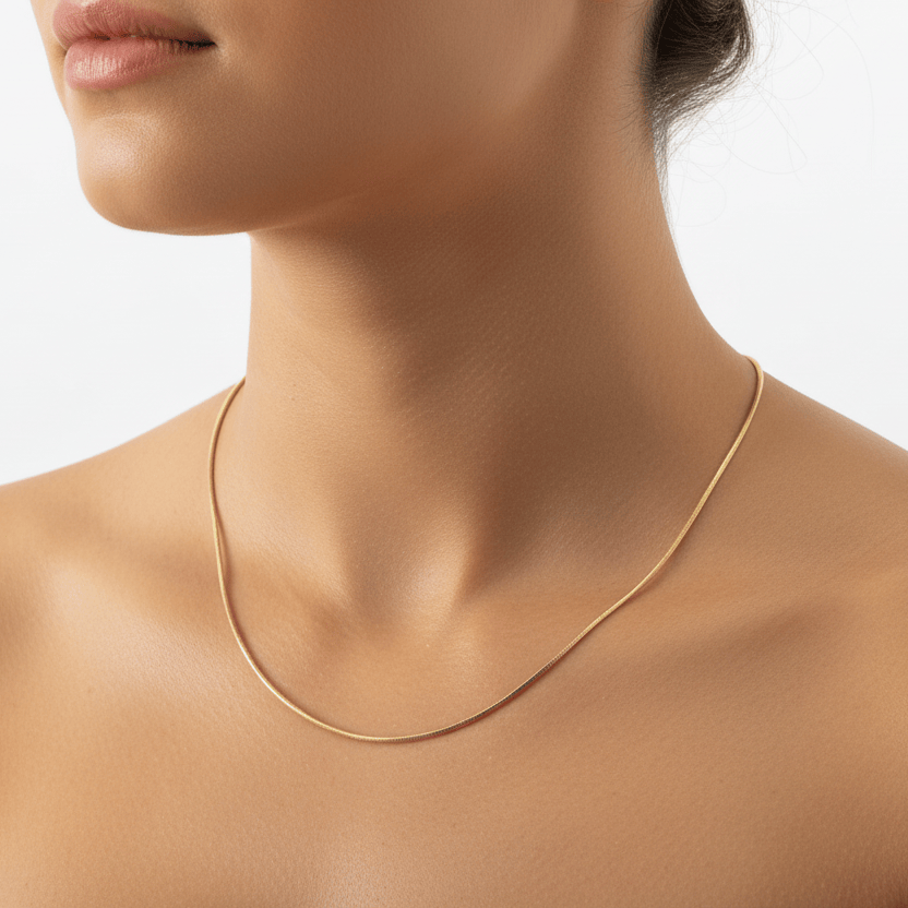 A close-up of a model's neck and upper chest wearing a delicate, thin gold chain necklace against a plain light background.