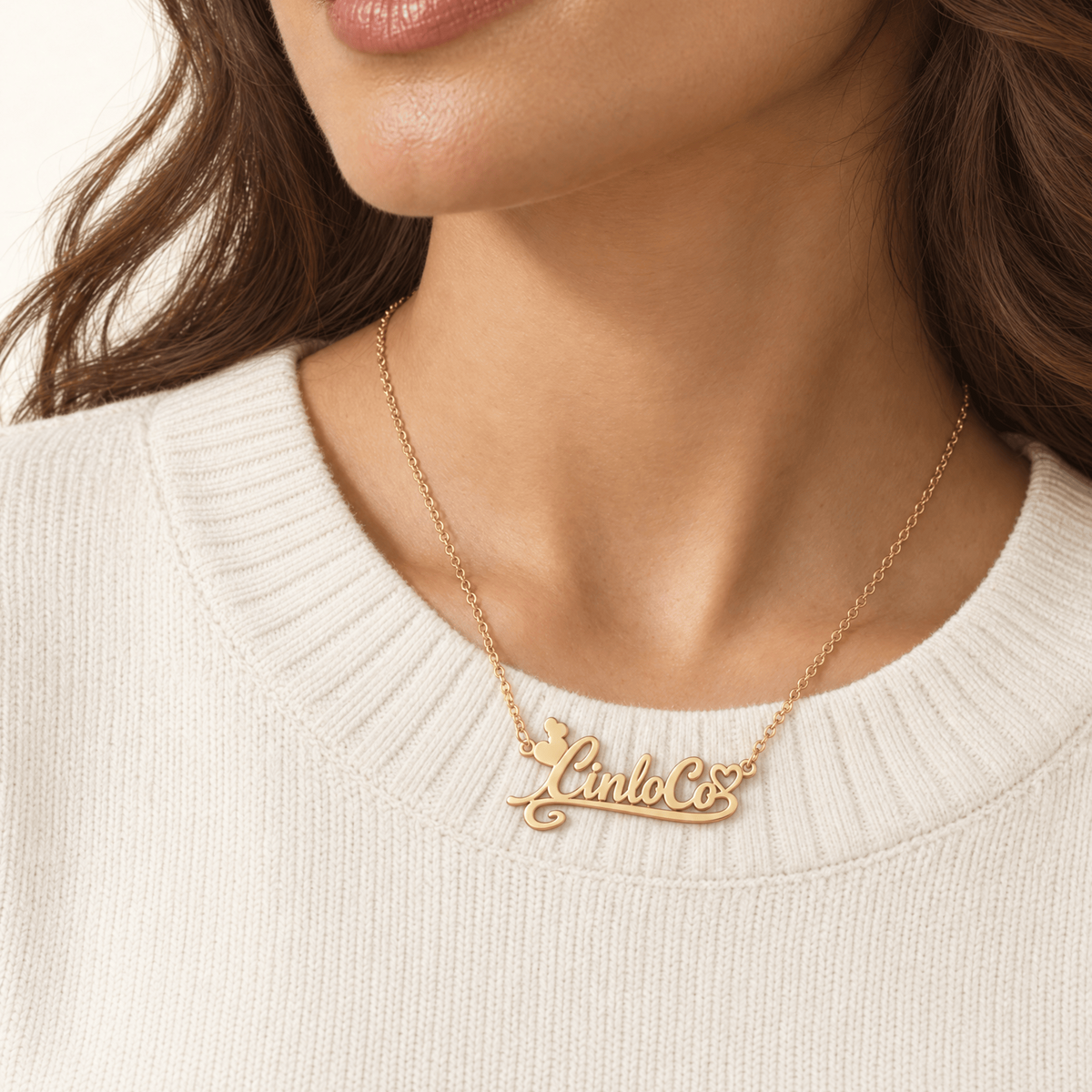 A close-up of a woman wearing a delicate gold script nameplate necklace that reads 'Lulu Co.' on a white ribbed knit sweater.