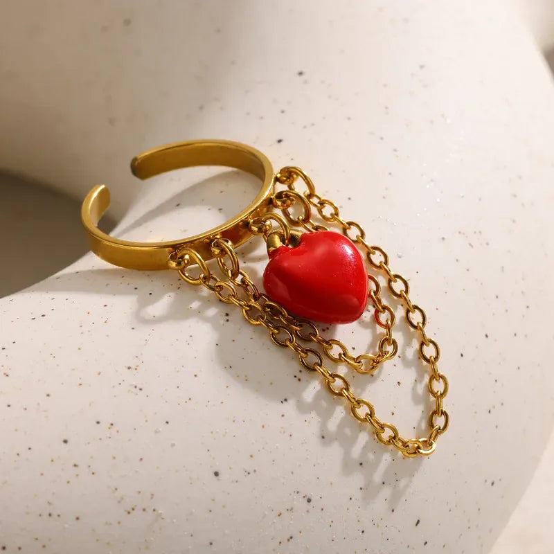 Gold ring with a red heart charm on a textured surface