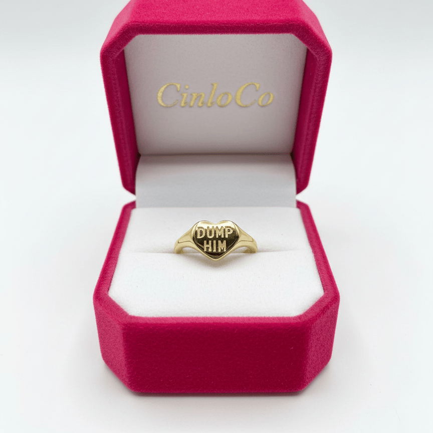 Gold ring with 'DUMP HIM' engraving in a pink 'Cinco Co.' box on a white background