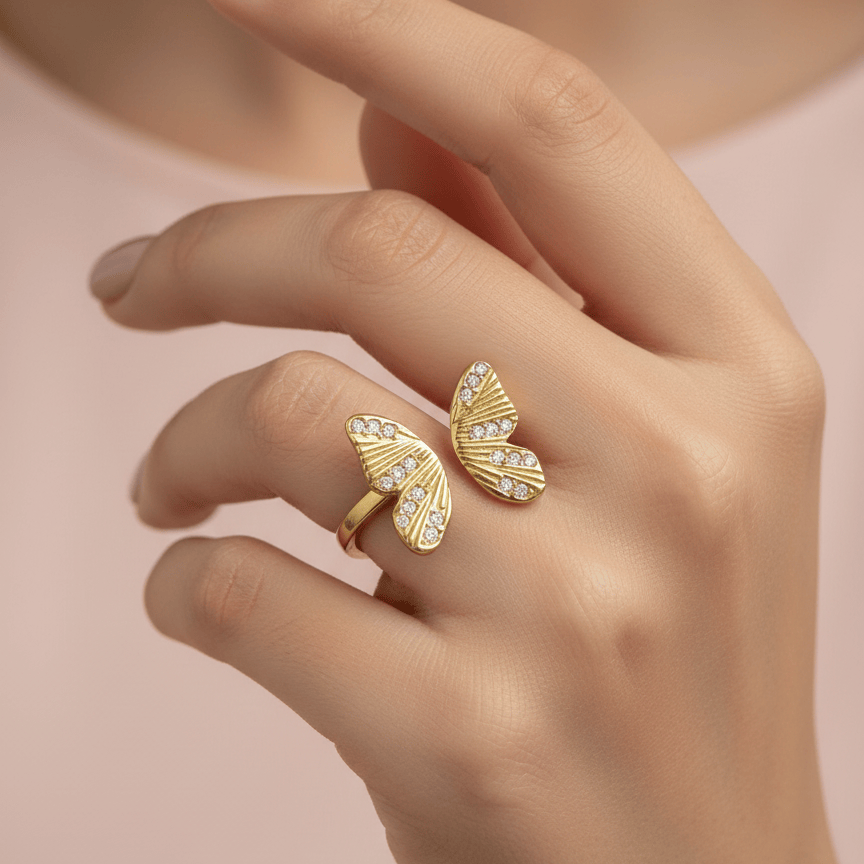 Gold ring with butterfly design on a hand against a soft pink background